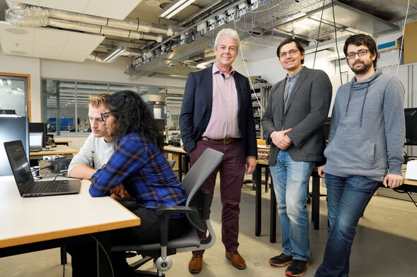 Paul van den Hof (links), Mircea Lazar (midden) en Maarten Schoukens (rechts) in het lab met studenten. Foto | Bart van Overbeeke
