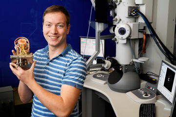 [Translate to English:] Wouter Verhoeven voor een elektronenmicroscoop met zijn bundelknippende resonator. Foto | Bart van Overbeeke