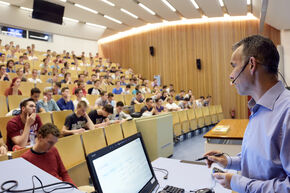 Collegezaal met docent, scherm op zwart. Foto | Bart van Overbeeke